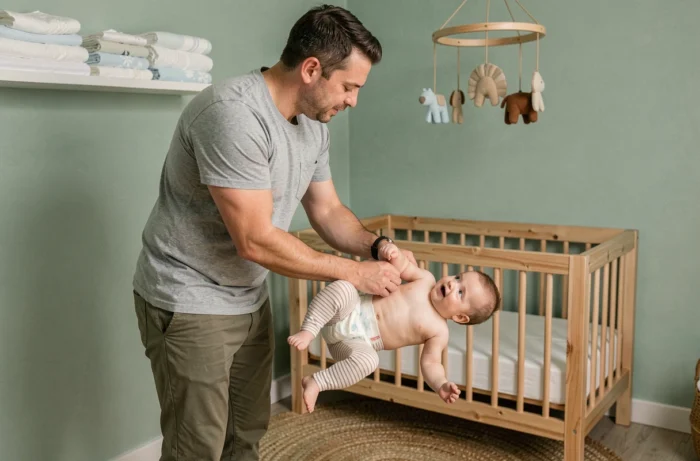 Père changeant la couche de son bébé sur une table à langer dans une chambre de bébé décorée en vert sauge